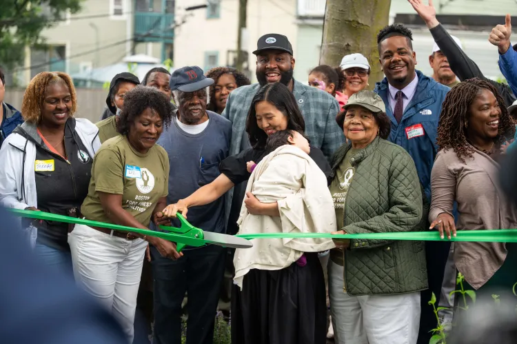 Mayor Wu of Boston holds a child while cutting a ribbon with a group of people