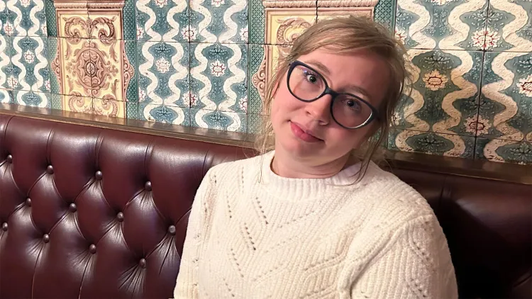 Person wearing glasses and a white sweater, sitting on a tufted leather bench.