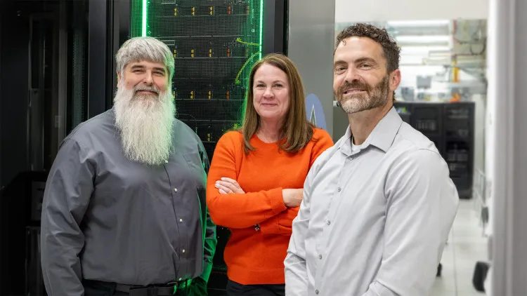 Three people posed in front of of a computing stack