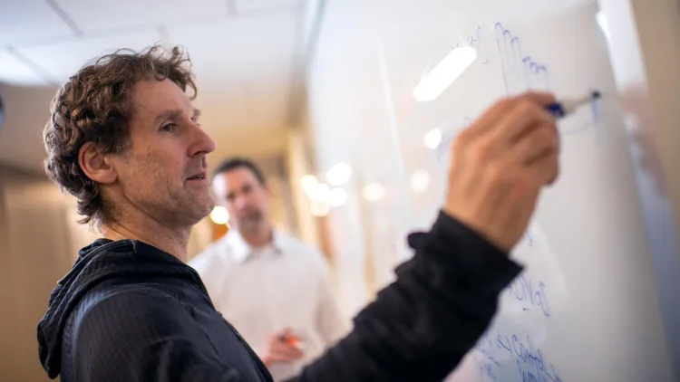 A professor writes out an equation on a white board