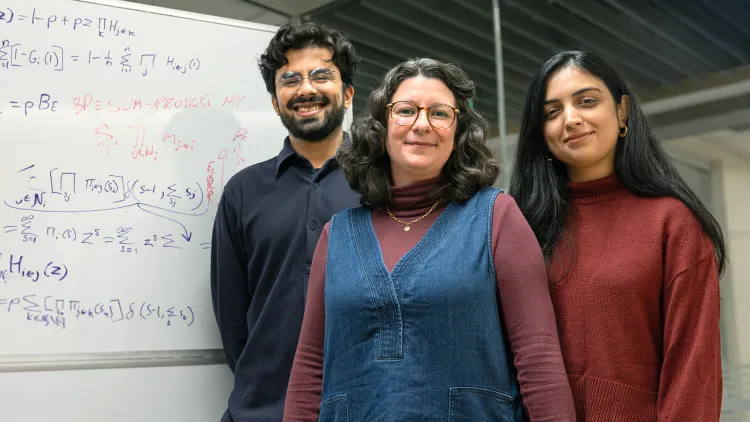 Three individuals posing in front of a white board