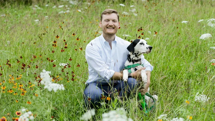 Person kneeling in a wildflower field while holding a dog.