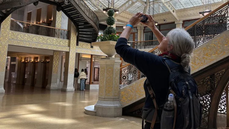 Person with a backpack taking a photo inside an ornate building with a grand staircase.