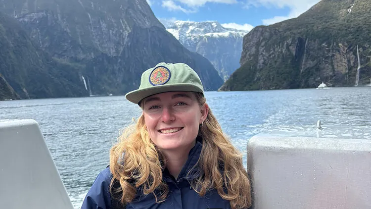 Student smiling on a boat with steep cliffs and water in the background.