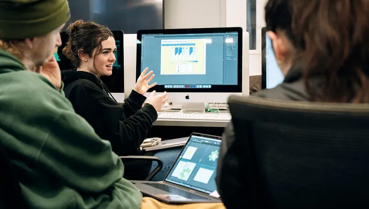 Students discuss a team project while working on their computers