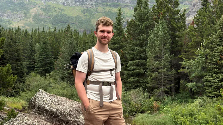 Person wearing a backpack standing in a forested mountain landscape.