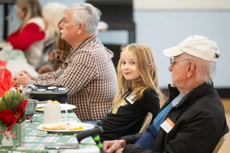 a little girl smiles during an intergenerational meal at her school