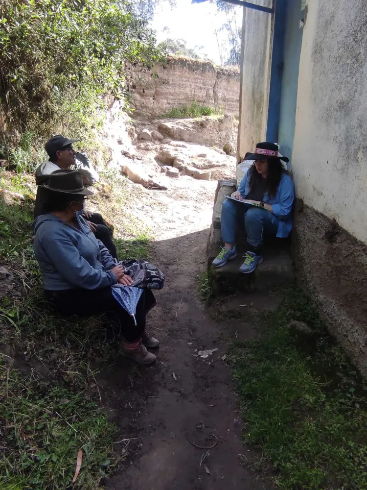 A photo of three people sitting in the shade of a building and talking. 