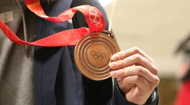A hand holding an Olympic bronze medal.