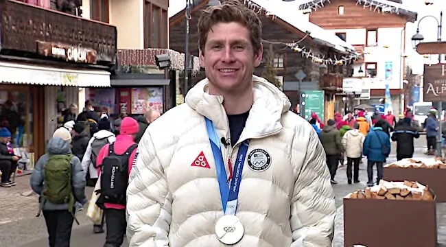 a man stands on a street wearing an Olympic medal