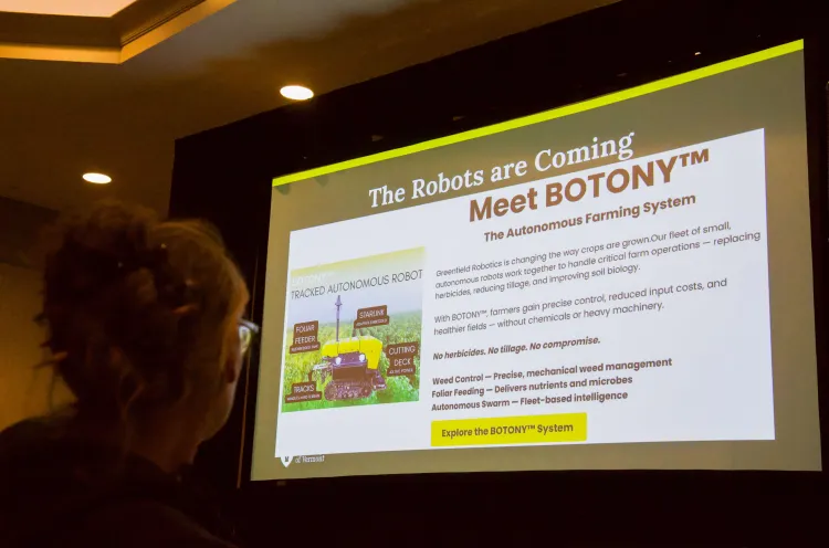 A powerpoint slide on a big screen that says "the robots are coming" and "Meet BOTONY." A person is looking toward the screen in the foreground of the image.