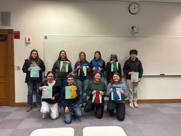 Ten young people standing in two rows holding green pieces of paper and ribbons