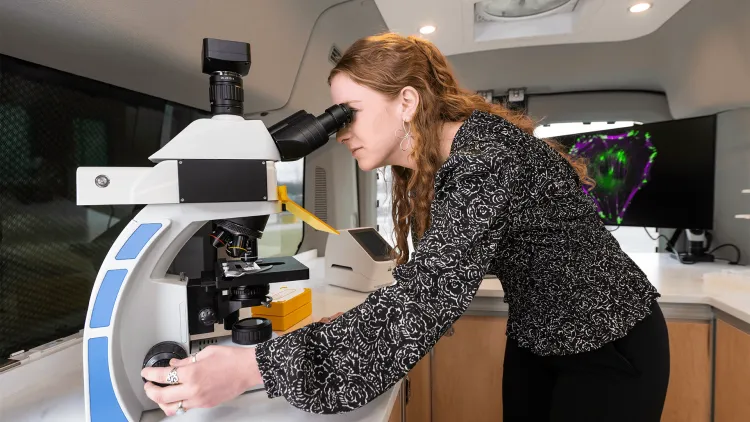 a person looking into a microscope in a lab inside a van with work space and equipment