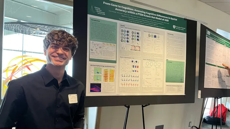 Hunter Holoubek standing in front of his presentation board that reads, “From Gene to Cognition: Assessing Cognitive Differences in Spatial Accuracy within a PTEN Knock Out Model of ASD”