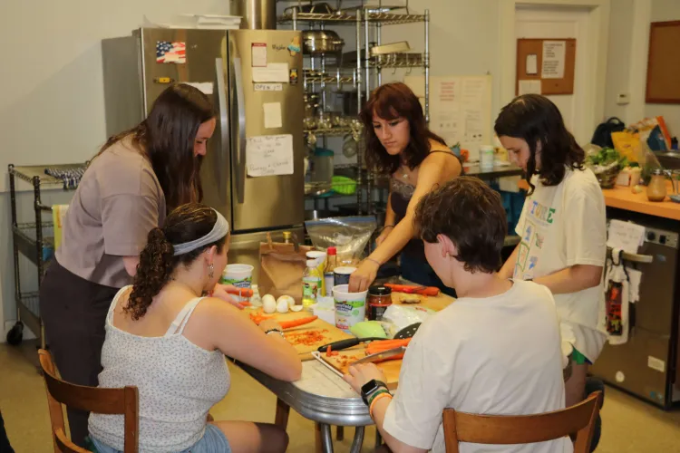 Five UVM Interns make a community meal together in a kitchen in White River Valley