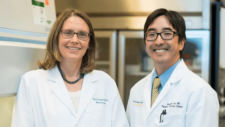 2 researchers in white coats smiling