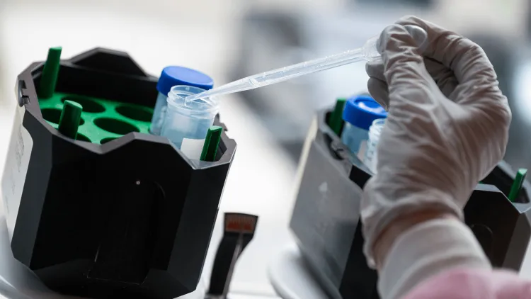 a gloved hand holding an eyedropper dripping into a test tube
