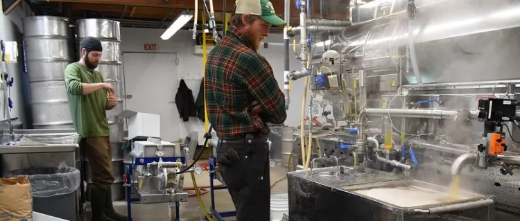 two men standing by a steaming, industrial evaporator, making maple syrup