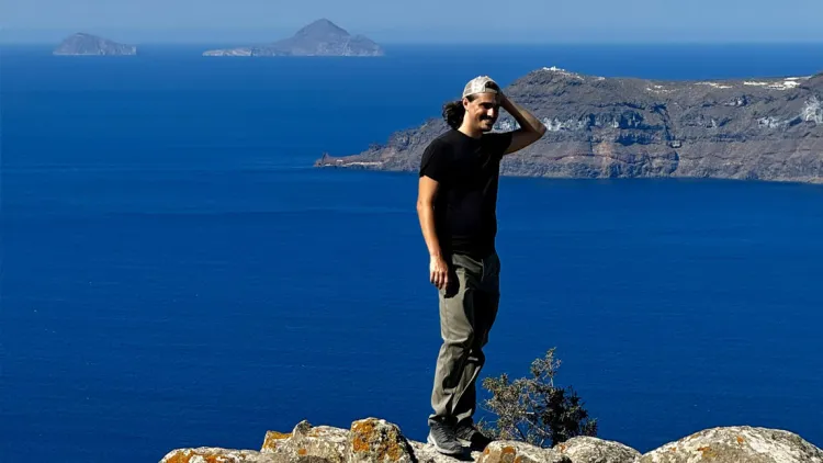 Person standing on a rocky cliff overlooking the ocean and distant islands.