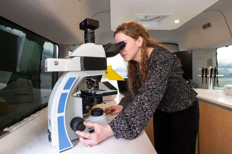 A woman in the UVM Cancer Center BioMobile lab looks into a microscope