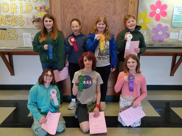Seven young people hold ribbons and papers.