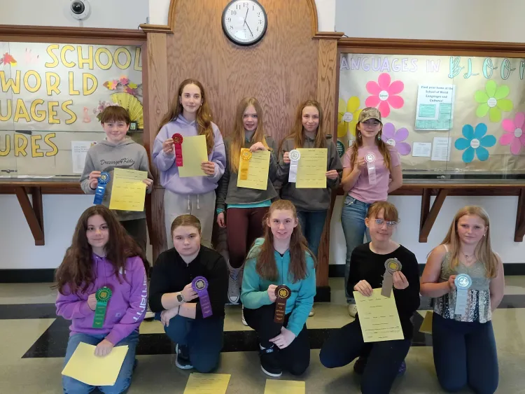 Ten young people standing in two rows holding green pieces of paper and ribbons