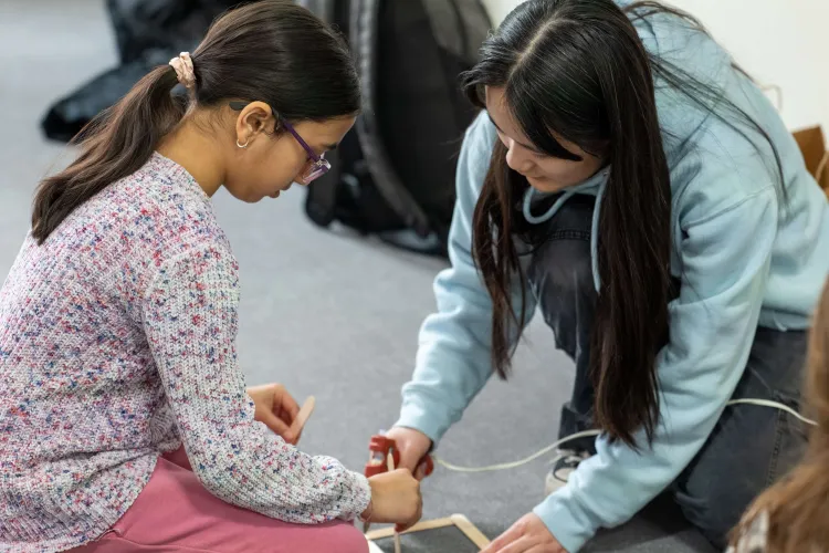 A photo of a young woman and a young girl working with popsicle sticks and a glue gun.