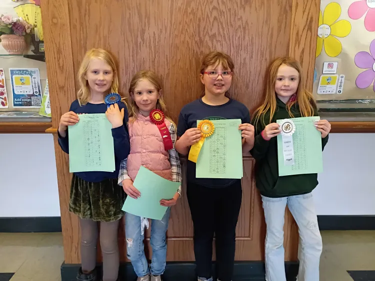 Four young people stand against a wall holding ribbons.