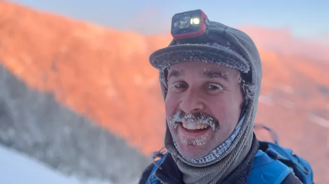 a man wearing mountaineering garb on a cold mountain trail