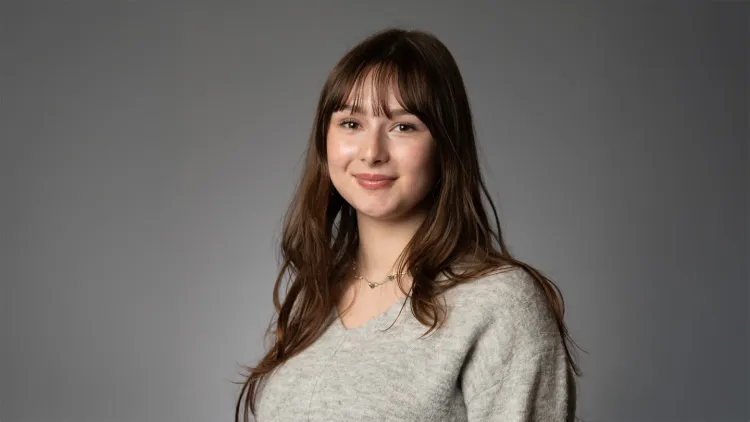 Person smiling in a studio portrait against a neutral background.