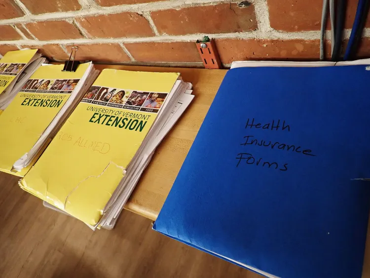 Four folders, three yellow and one blue, that say things like University of Vermont Extension and health insurance forms on them.