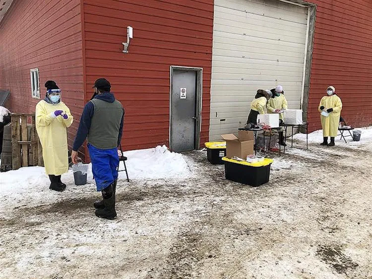 People in personal protective equipment including gowns and face masks stand outside a red barn