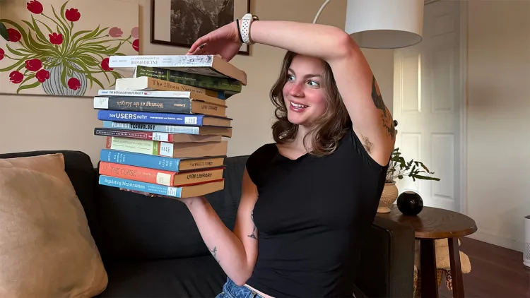 Young woman in black t-shirt holding a stack of books in a living room