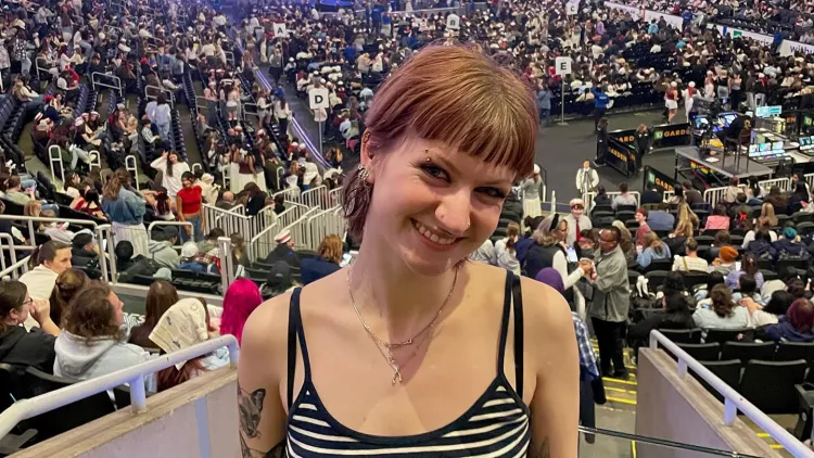 Person smiling in a crowded arena with a stage and large audience in the background.