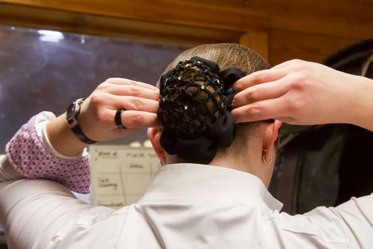 A person pulls a sparkly bun cover on their head, seen from the back