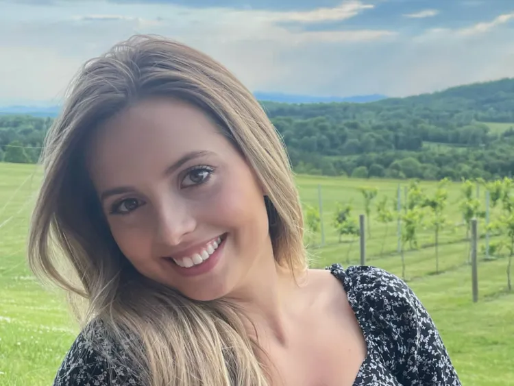 person sitting in a rural mountain setting smiles at camera