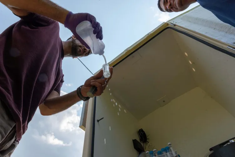 A person pouring a bottle of water into a vial with another person looking on. The photo is made from below the people. 