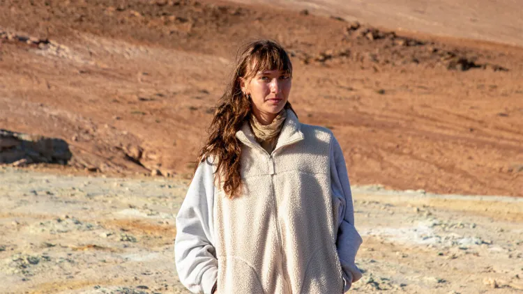 Young woman in white jacket with long brown hair standing in front of arid landscape