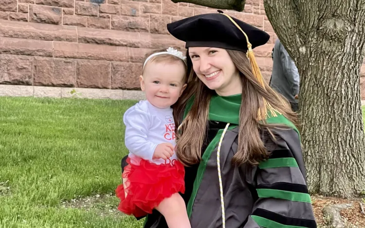 Person holding a toddler while in a graduation cap and gown