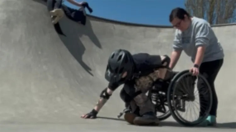 Two young people, on in wheelchair, in skate park