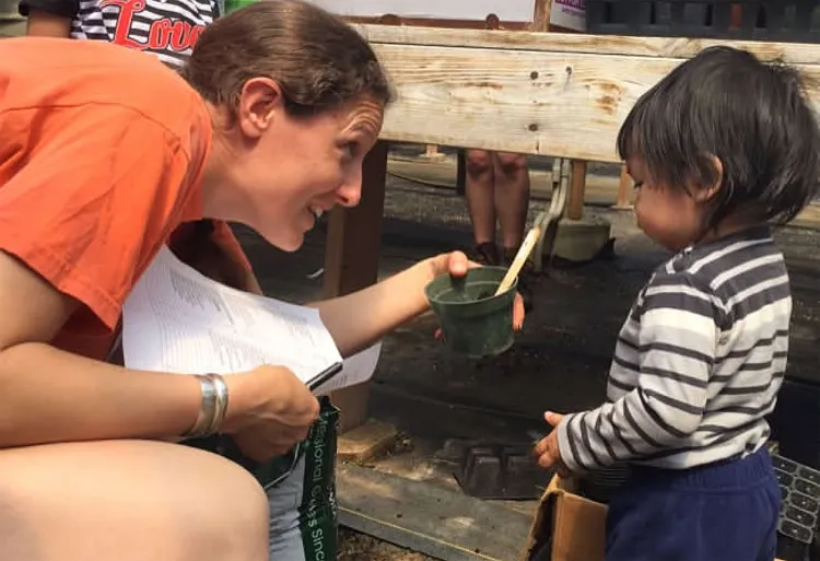 A woman holds up a small planting pot to a young boy.