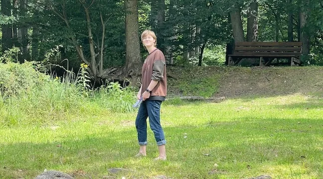 a woman walking in a field with trees in the background