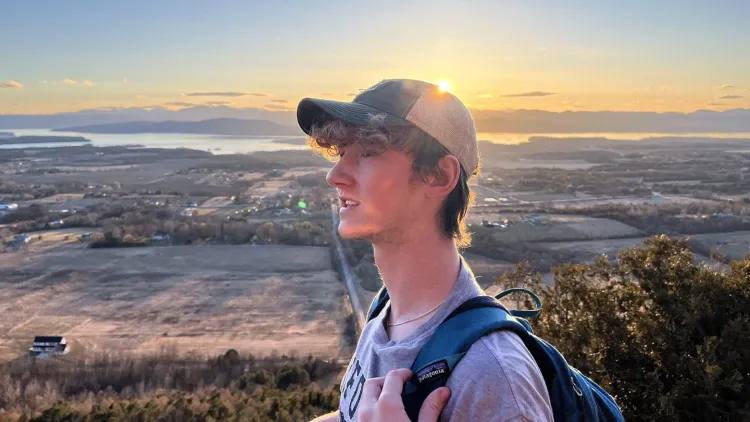 Person on a mountain with a sunset and scenic view in the background.