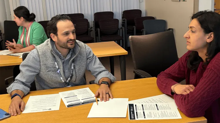 2 people sitting at a table with a person in the background