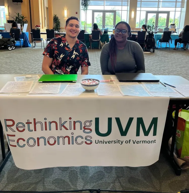 Two people, a man and woman, sit at a table with a banner that reads "Rethinking Economics."