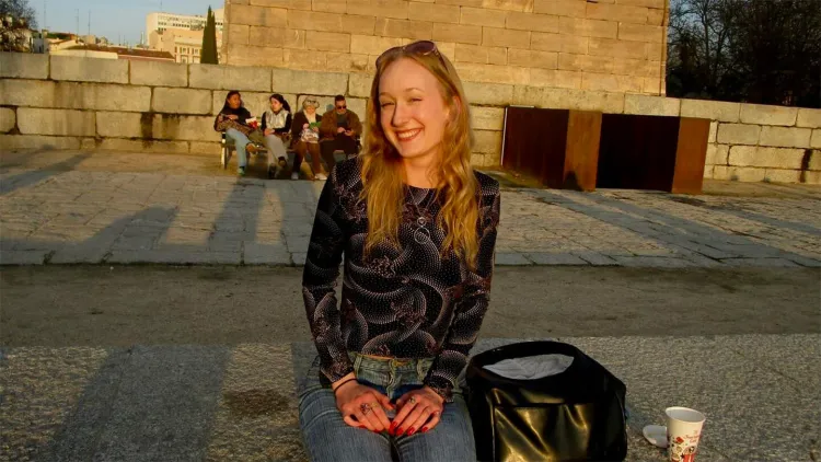 Young woman with long blonde hair smiling and sitting on bench on a sunny day