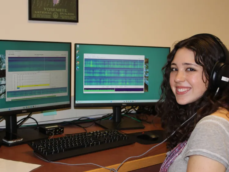 Student Sadie Dowe siting in front of two computer monitors, wearing headphones