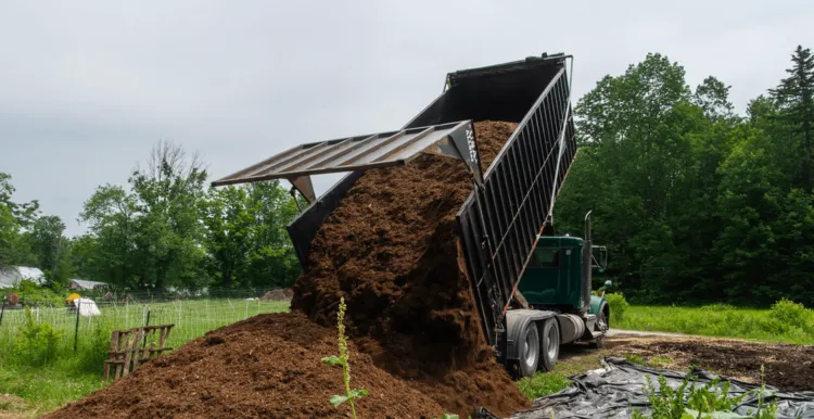 Dump truck pours out bed of mulch on a farm site