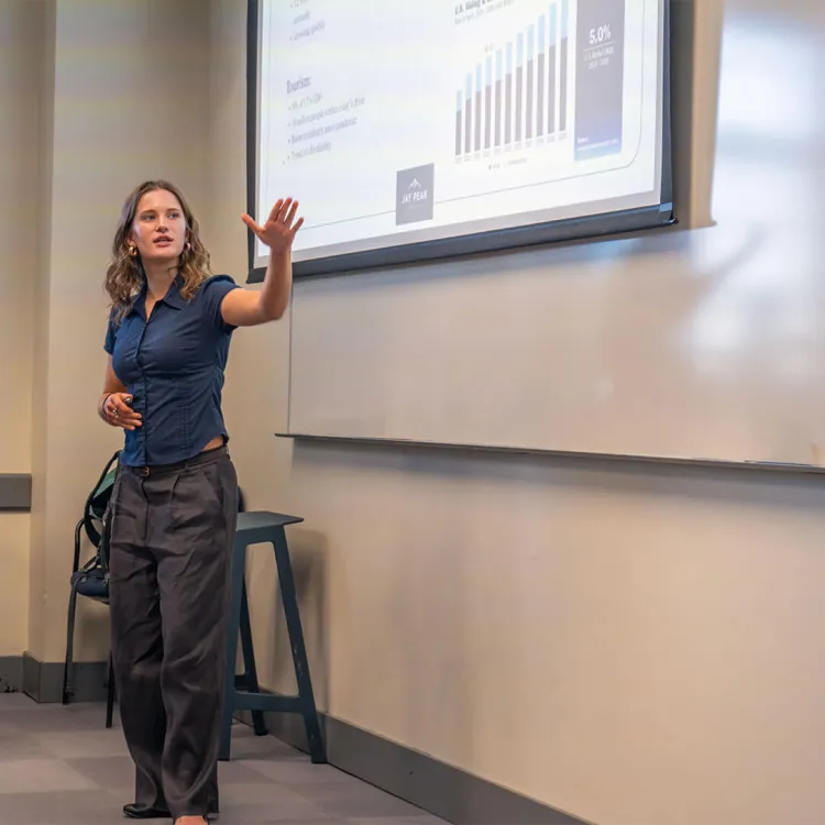 A student presents in front of a power point projection to a panel of judges at the UVM Business Pitch competition 2026