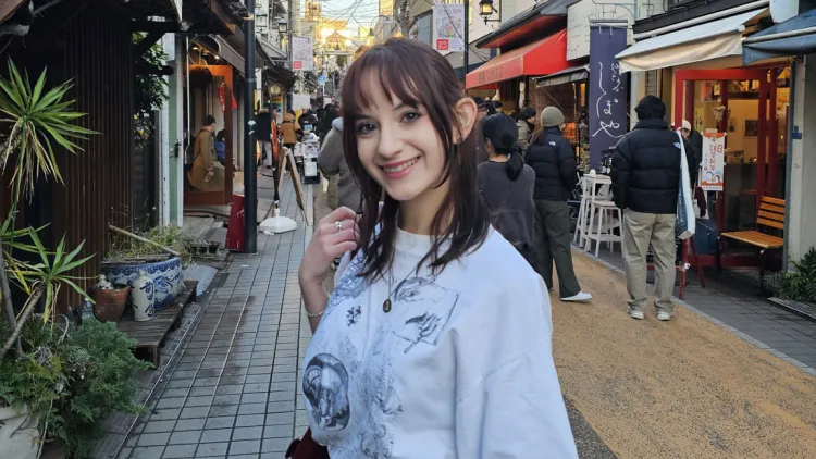 Person smiling on a narrow street lined with small shops and pedestrians.